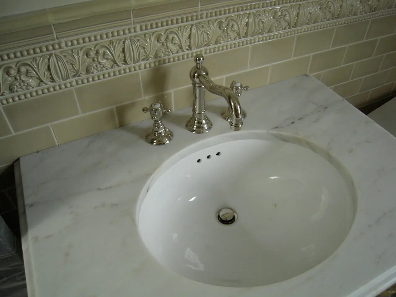 In the foreground of this image, there is a marble sink and taps on it. In the background, there is...