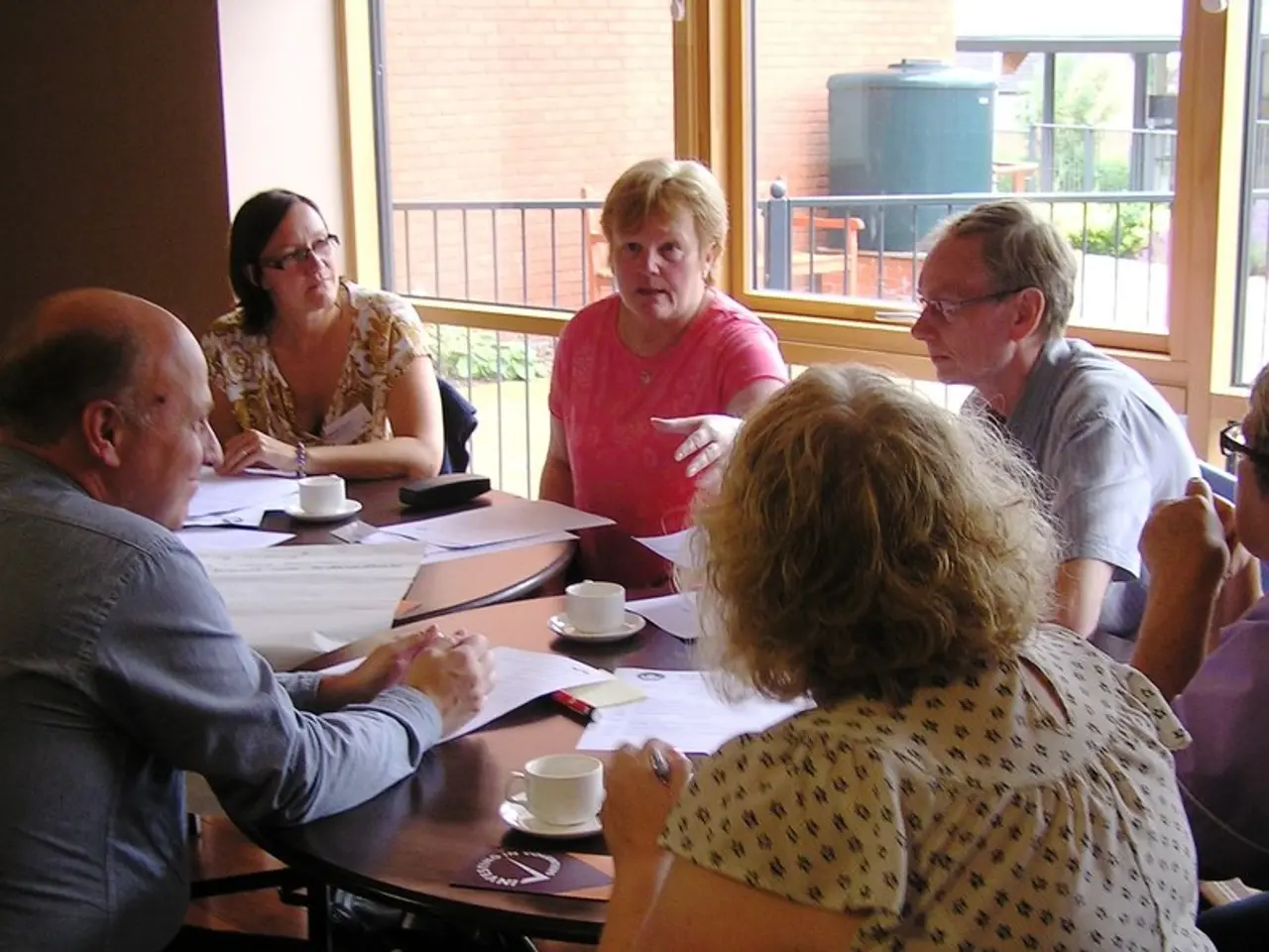 As we can see in the image there are 7 people sitting around table and discussing. On table there...