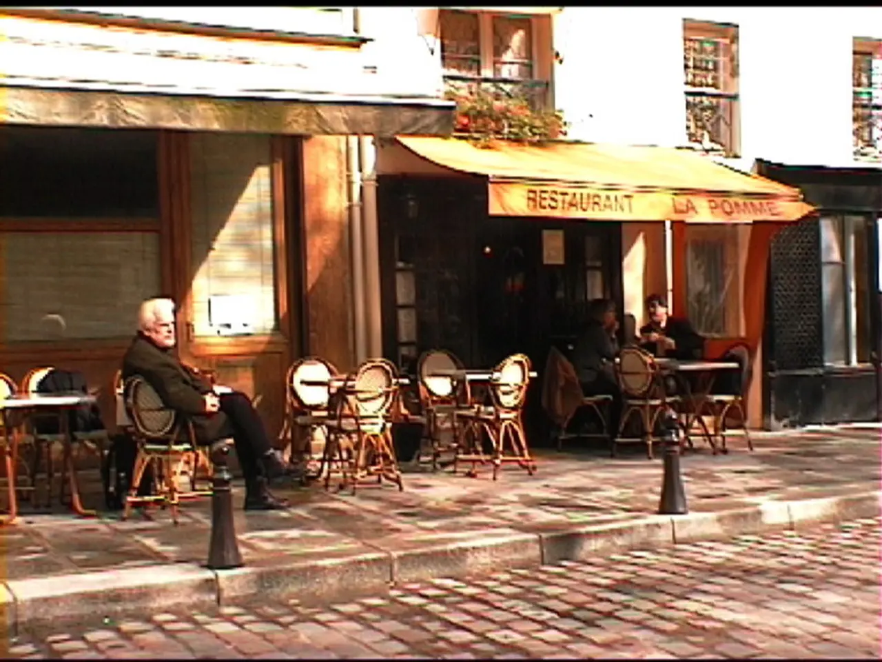 In the image we can see there is a man who is sitting on chair and there are tables and chair on...