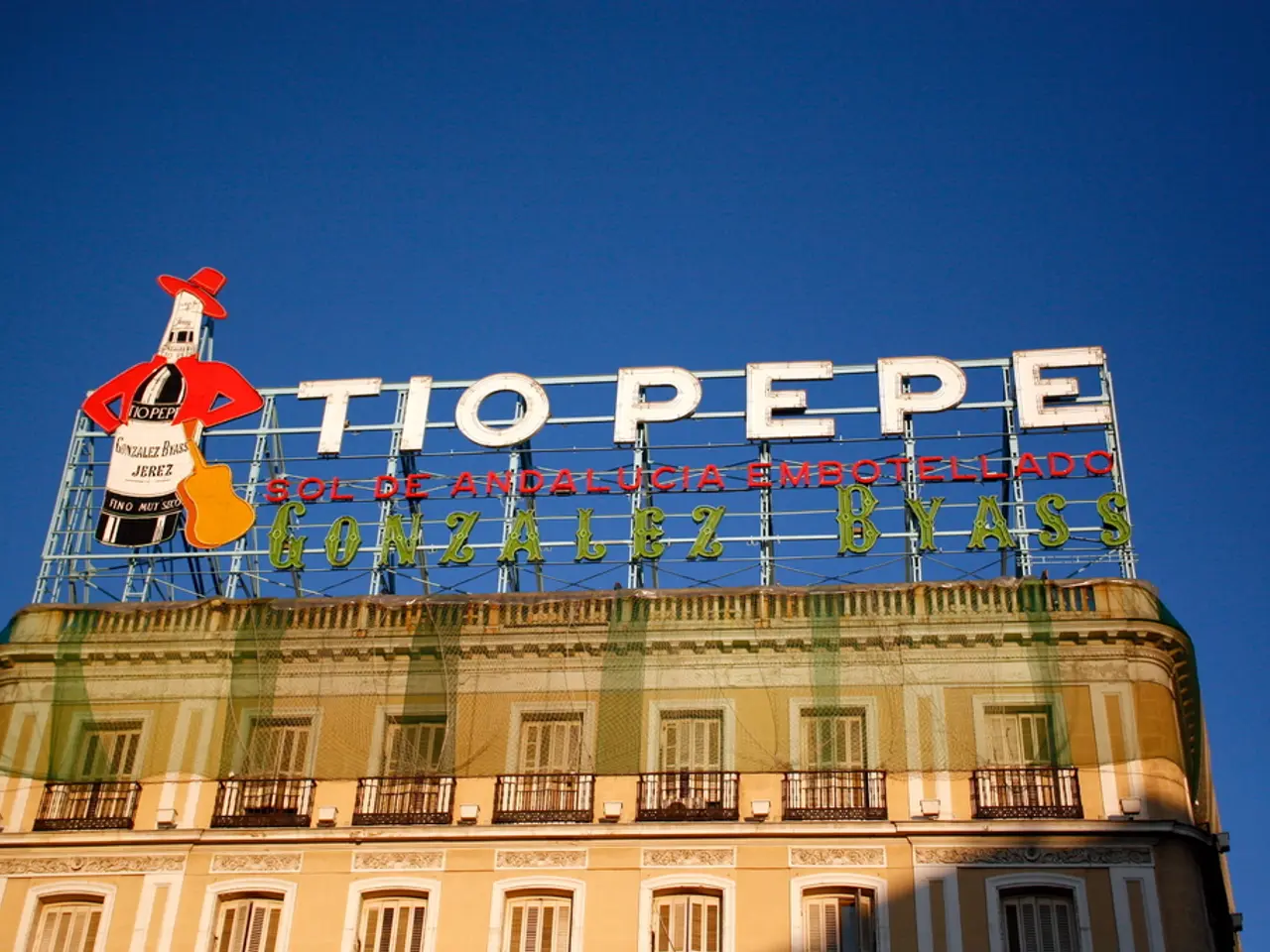 In this image there is a building with net and name boards , and in the background there is sky.