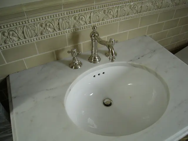 In the foreground of this image, there is a marble sink and taps on it. In the background, there is...