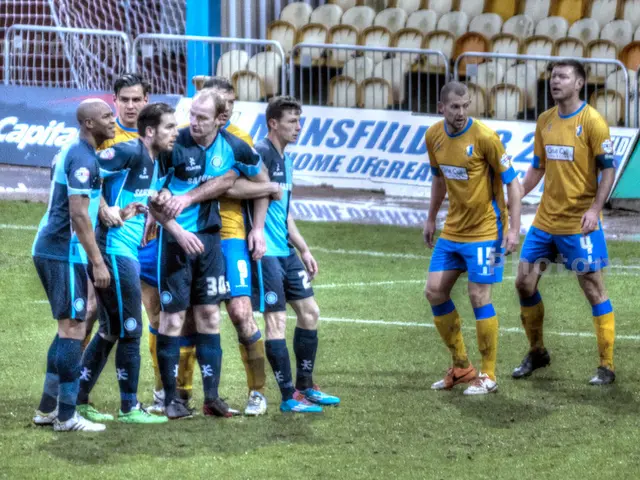 There are men those who are standing on the grassland and there are posters, chairs and a net in...